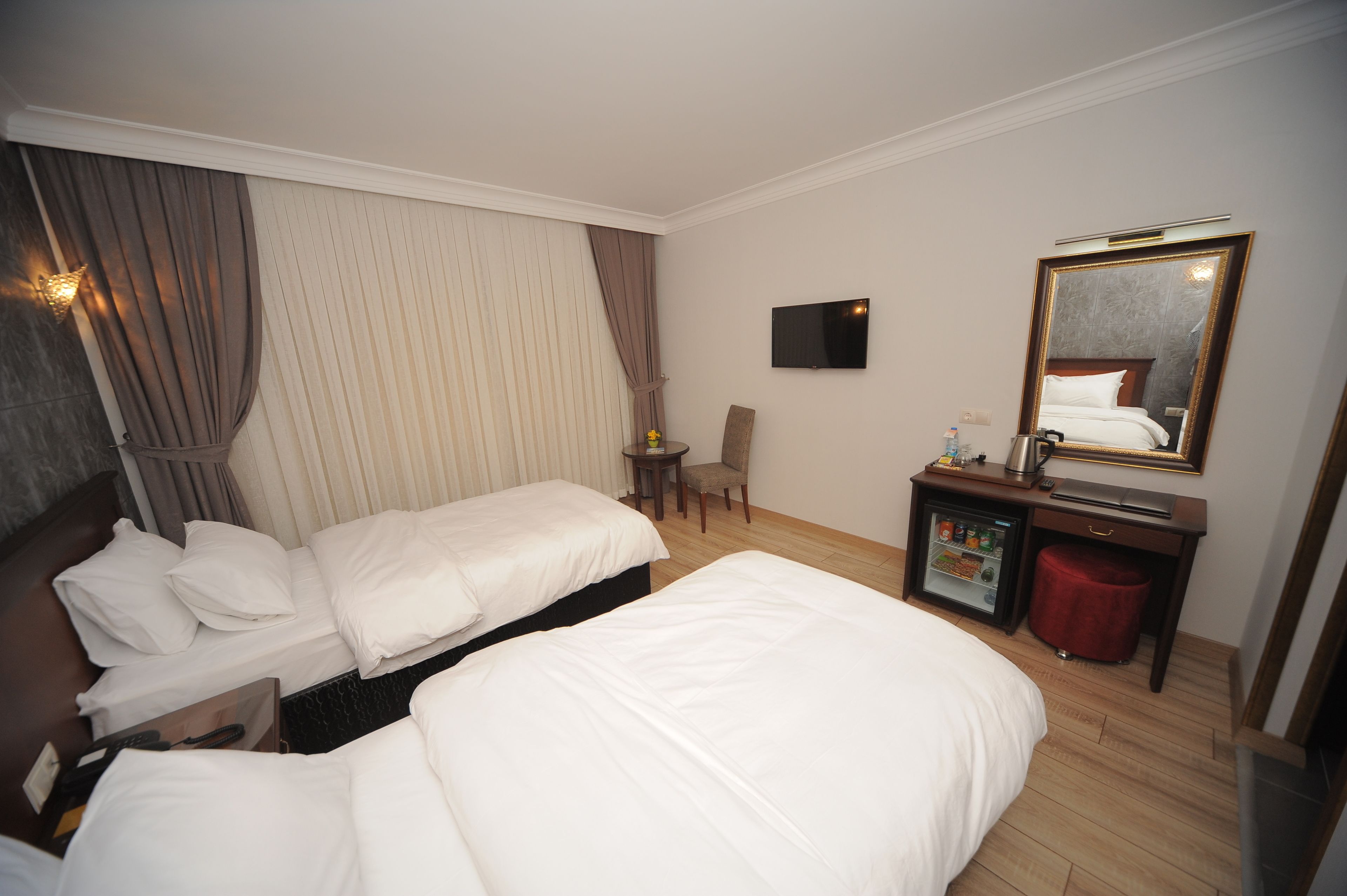 Habitación de hotel con dos camas, televisión, espejo, escritorio pequeño con refrigerador y una silla.