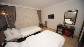 Habitación de hotel con dos camas, televisión, espejo, escritorio pequeño con refrigerador y una silla.