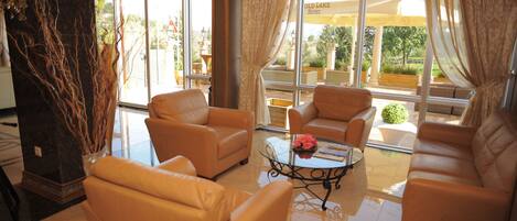 A spacious lounge area with leather sofas, a glass coffee table, and large windows offering a view of the outdoor seating area.