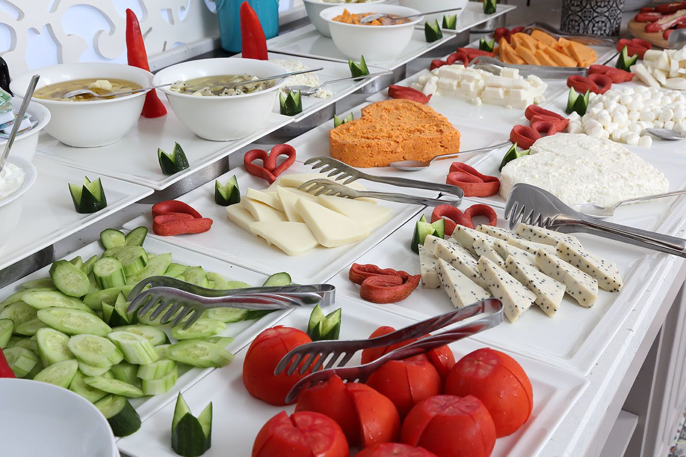 A buffet with various food items including sliced cucumbers, tomatoes, cheese, and a variety of other dishes.