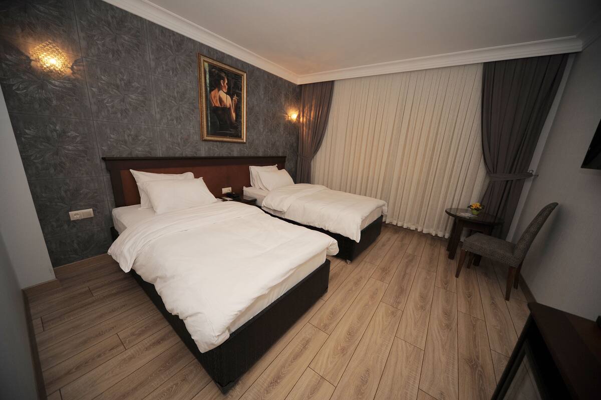 A hotel room with two beds, a wooden floor, a painting on the wall, and a small table with a chair.