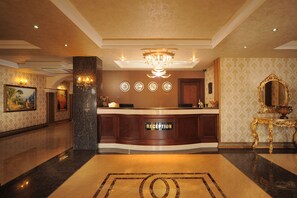 A reception area with a marble floor, a chandelier, a reception desk, and a mirror on the right. - Golden Lake Hotel (Adana)