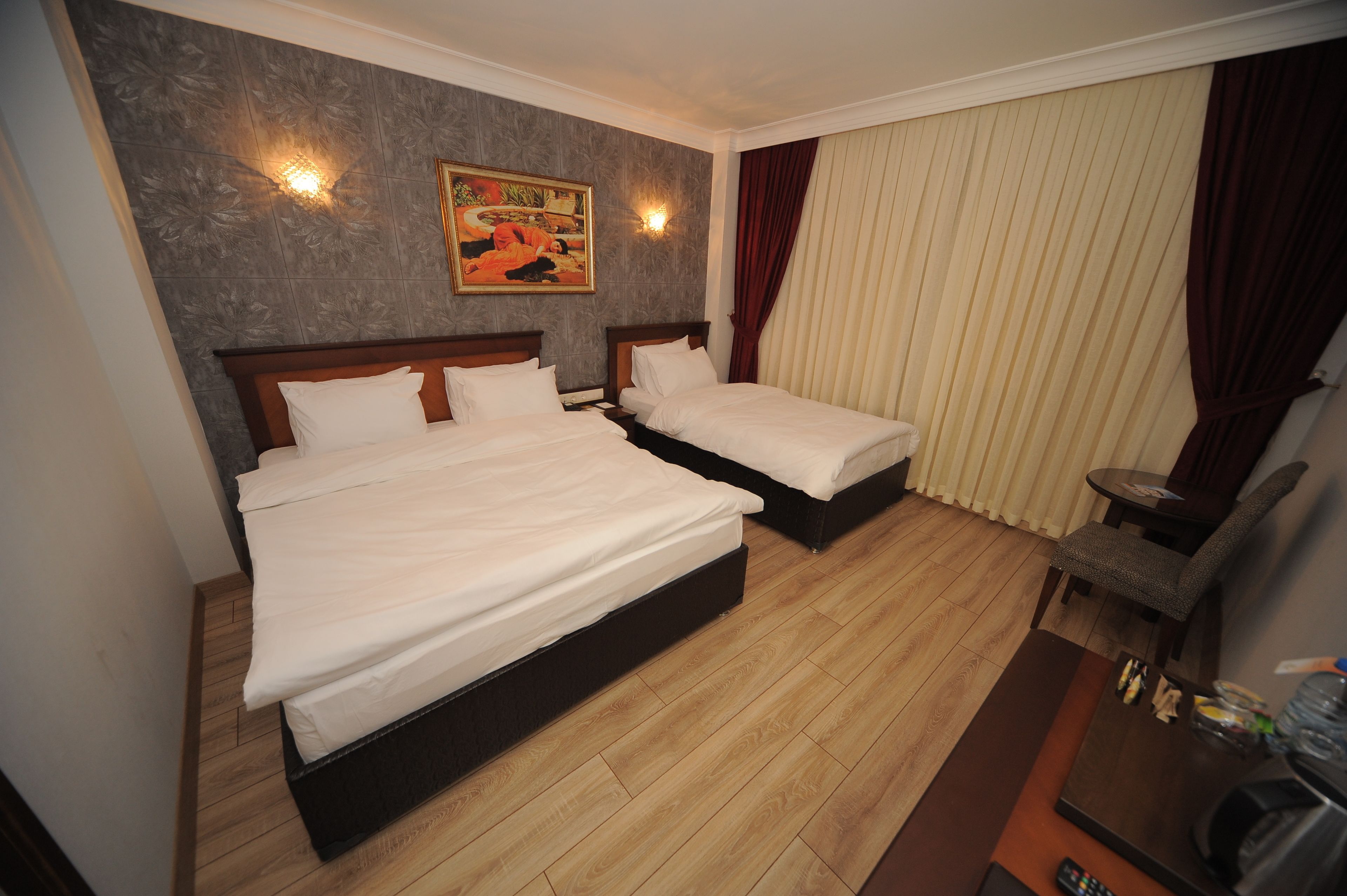 A hotel room with two beds, a wooden floor, a painting on the wall, and a desk with a chair.