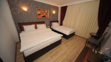 A hotel room with two beds, a wooden floor, a painting on the wall, and a desk with a chair.
