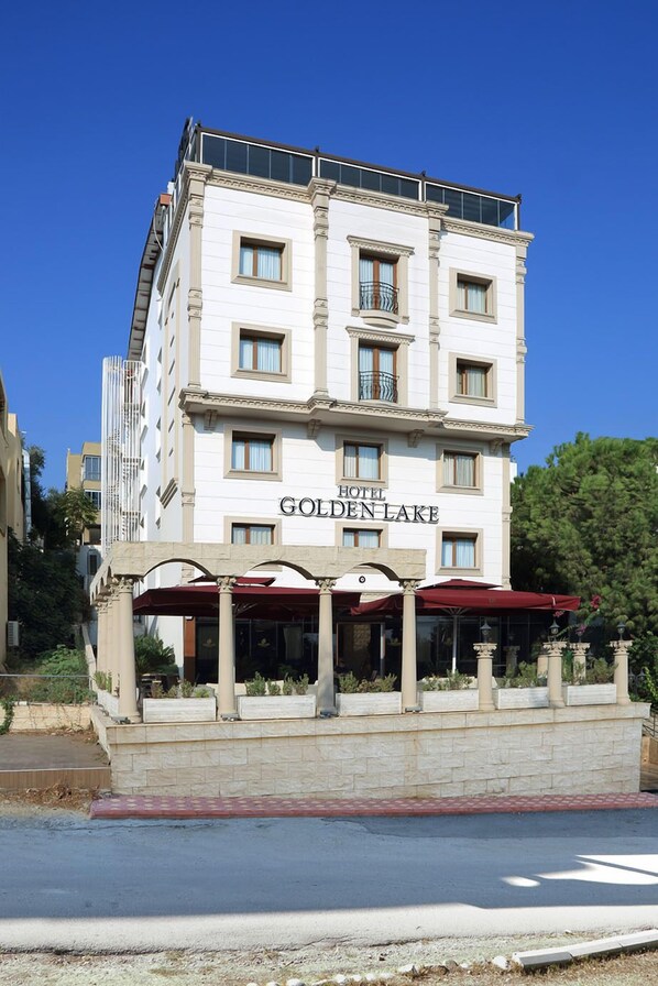 A multi-story hotel with a classic architectural style, featuring a prominent entrance with a red awning and columns. - Golden Lake Hotel (Adana)