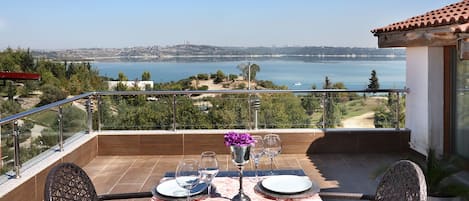A balcony with a table set for two, overlooking a coastal landscape.