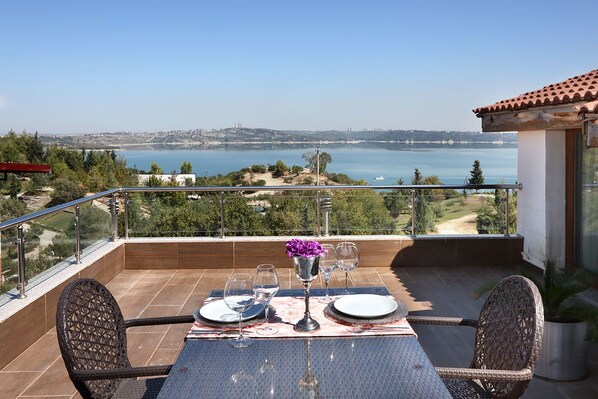 A balcony with a table set for two, overlooking a coastal landscape.