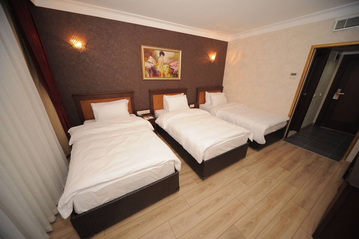 A hotel room with three single beds, a painting on the wall, and a wooden floor.
