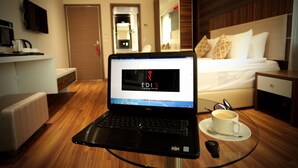 A laptop on a glass table in a hotel room with a bed, bedside table, and a cup of coffee. - Edis Premier Hotel (Adana)