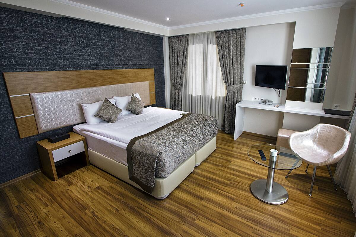 A hotel room with a bed, bedside table, desk, chair, and a TV.