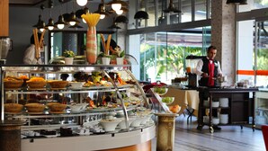 A buffet area with various food items displayed in bowls and containers, a waiter serving food, and a view of the outdoors through large windows. - Yol Is Holiday Adana (Adana)