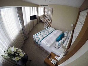 Una camera d'albergo con un letto, una televisione, una scrivania con il telefono e un vaso di fiori.
