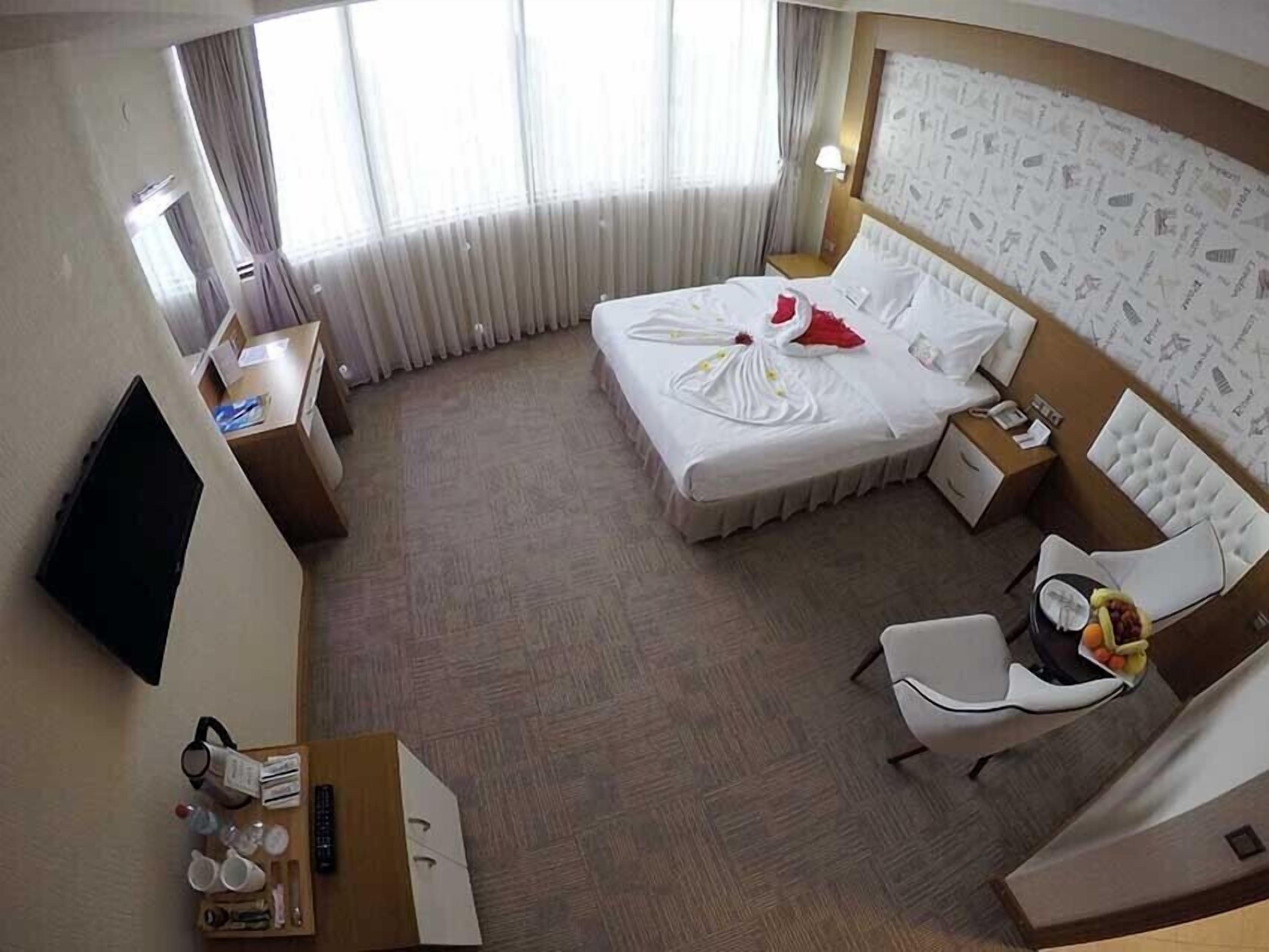 Una habitación de hotel con una cama grande, un escritorio con silla, televisión y ventana con cortinas.