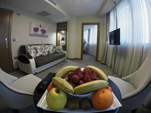 Ett vardagsrum med en soffa, ett soffbord med frukt på, en tv och en fjärrkontroll.