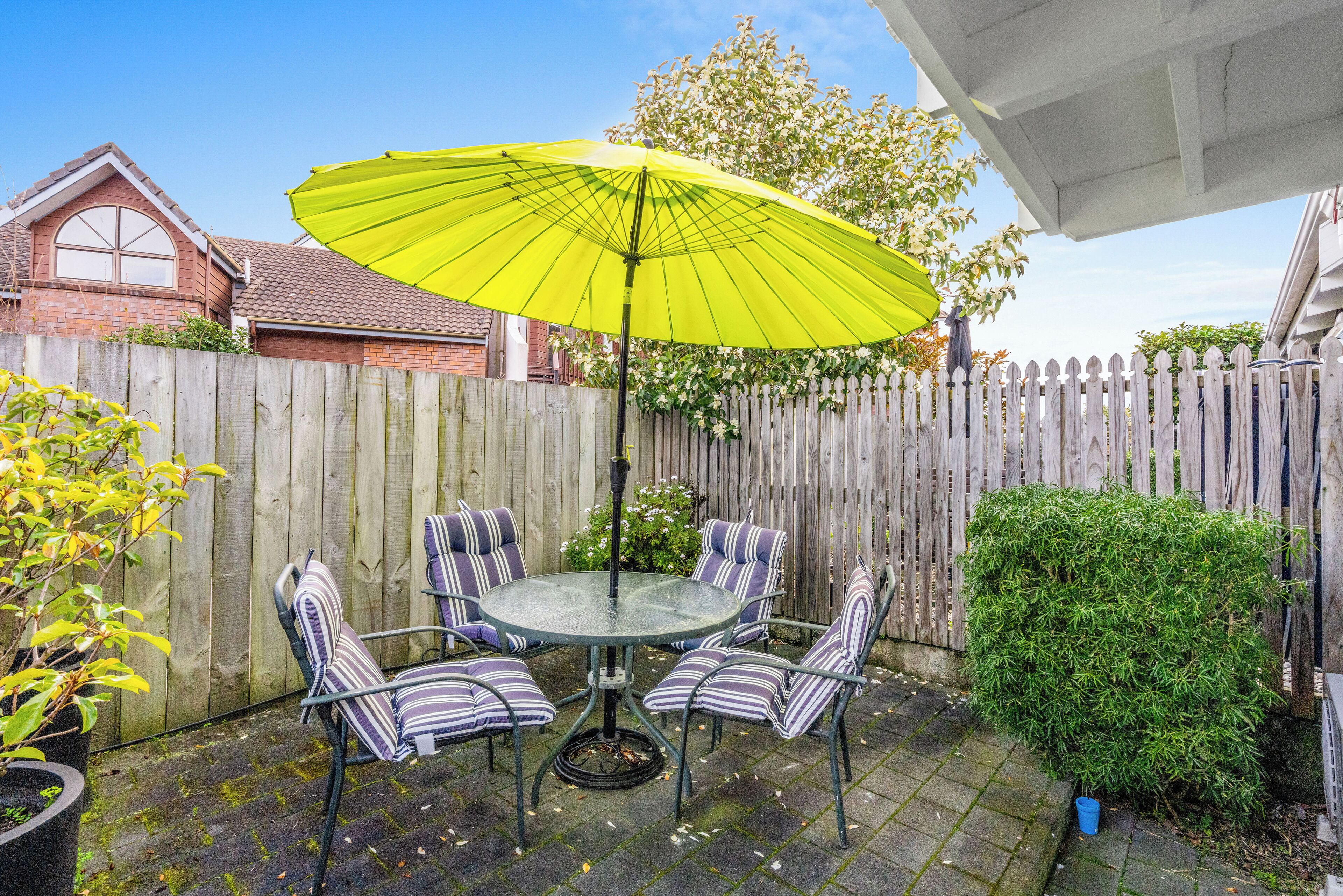 A round glass table with striped chairs and a bright yellow umbrella.