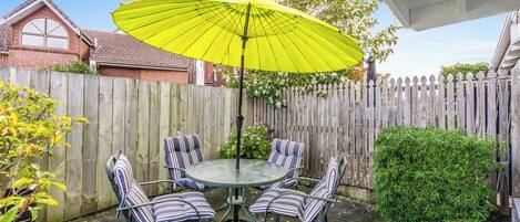A round glass table with striped chairs and a bright yellow umbrella.