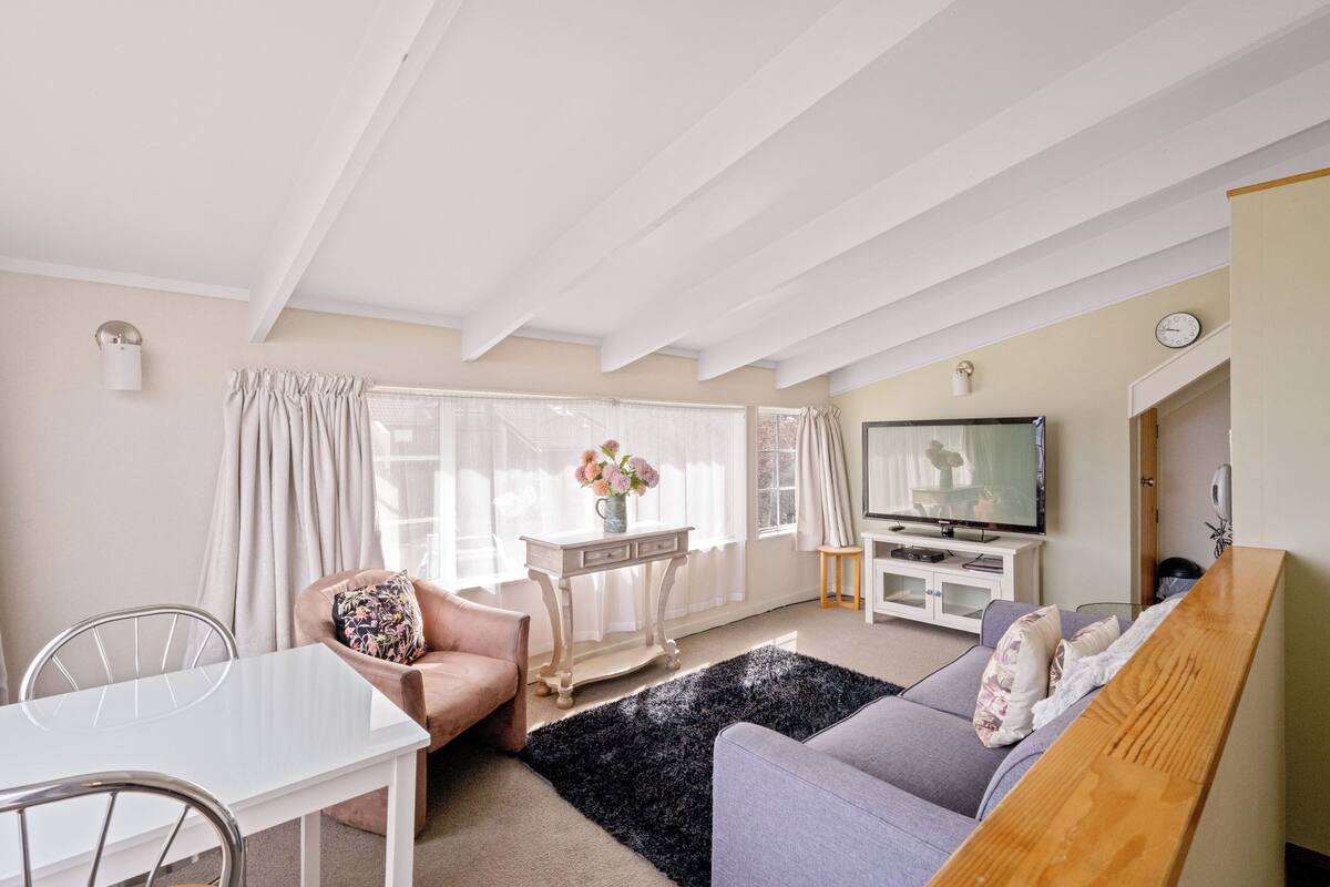 Een woonkamer met een wit plafond, een grijze bank, een witte tv-meubel en een eettafel met stoelen.