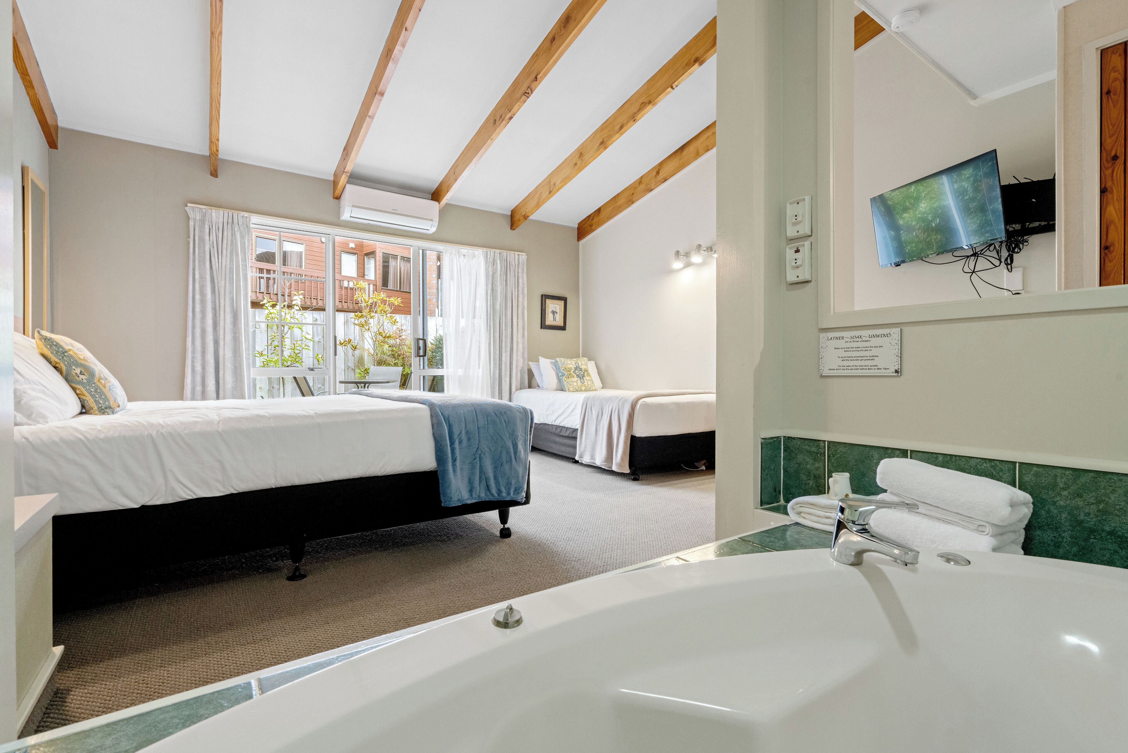 A hotel room with two beds, a large bathtub, and a view of a building outside.