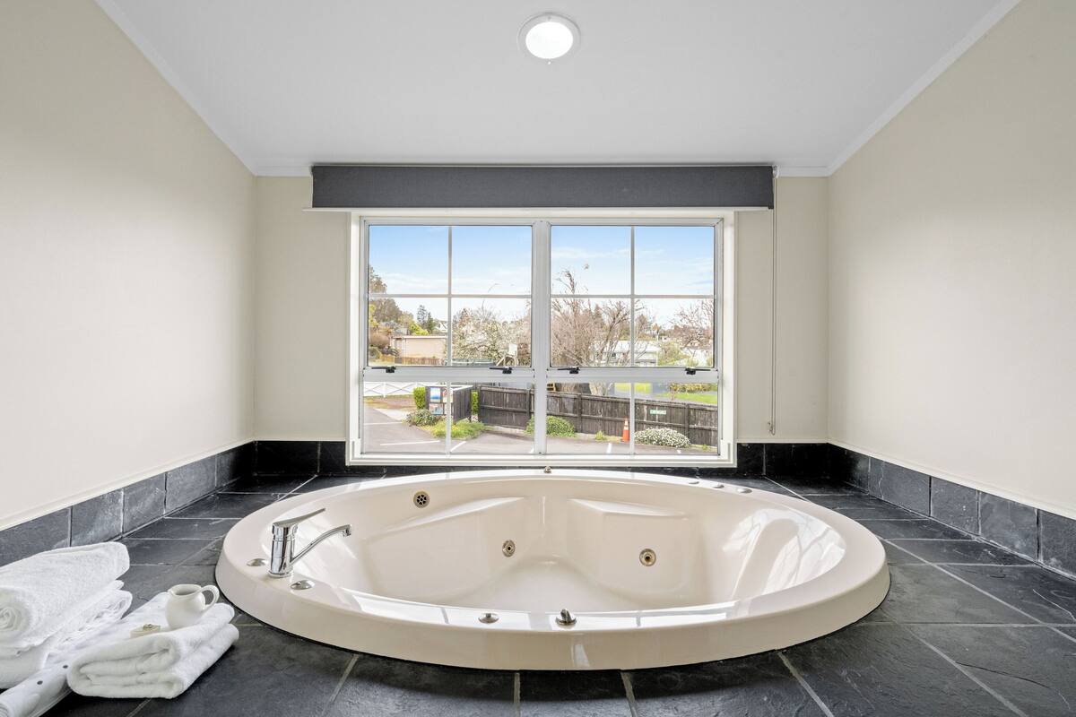 Een moderne badkamer met een vrijstaand ligbad, een raam met uitzicht en netjes opgevouwen handdoeken op de vloer.