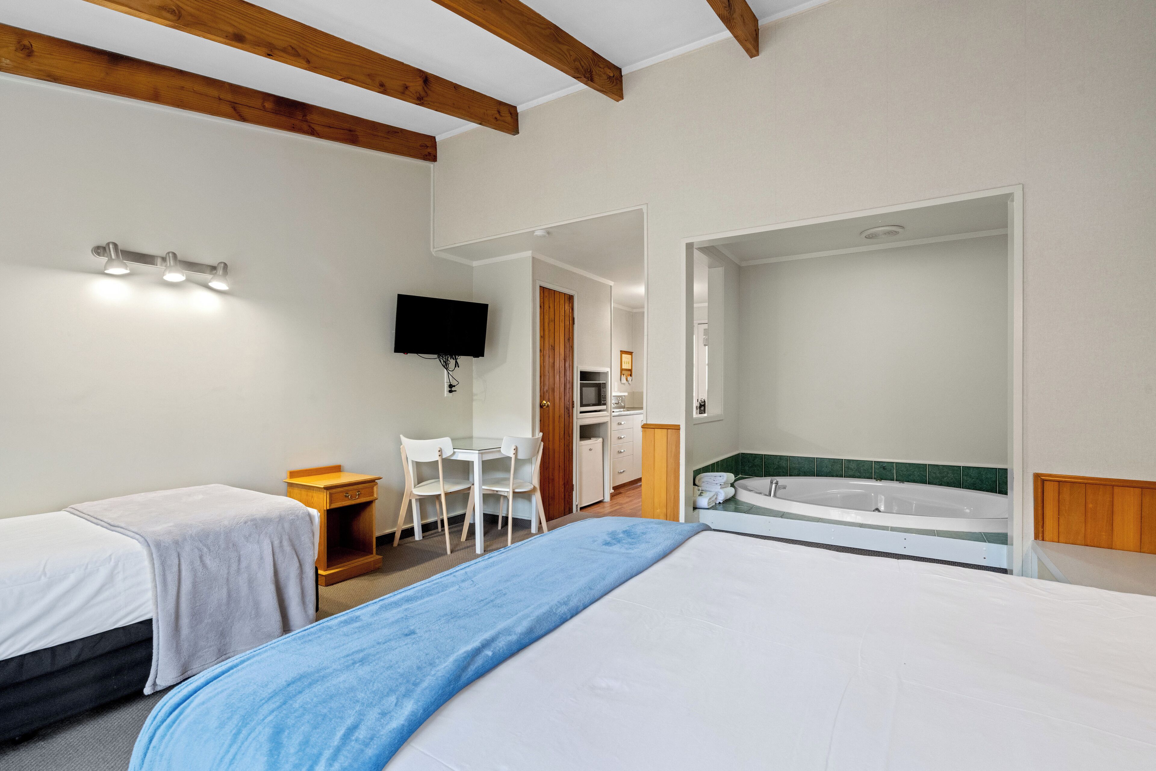A hotel room with two beds, a desk, a TV, a kitchenette, and a bathroom with a bathtub.