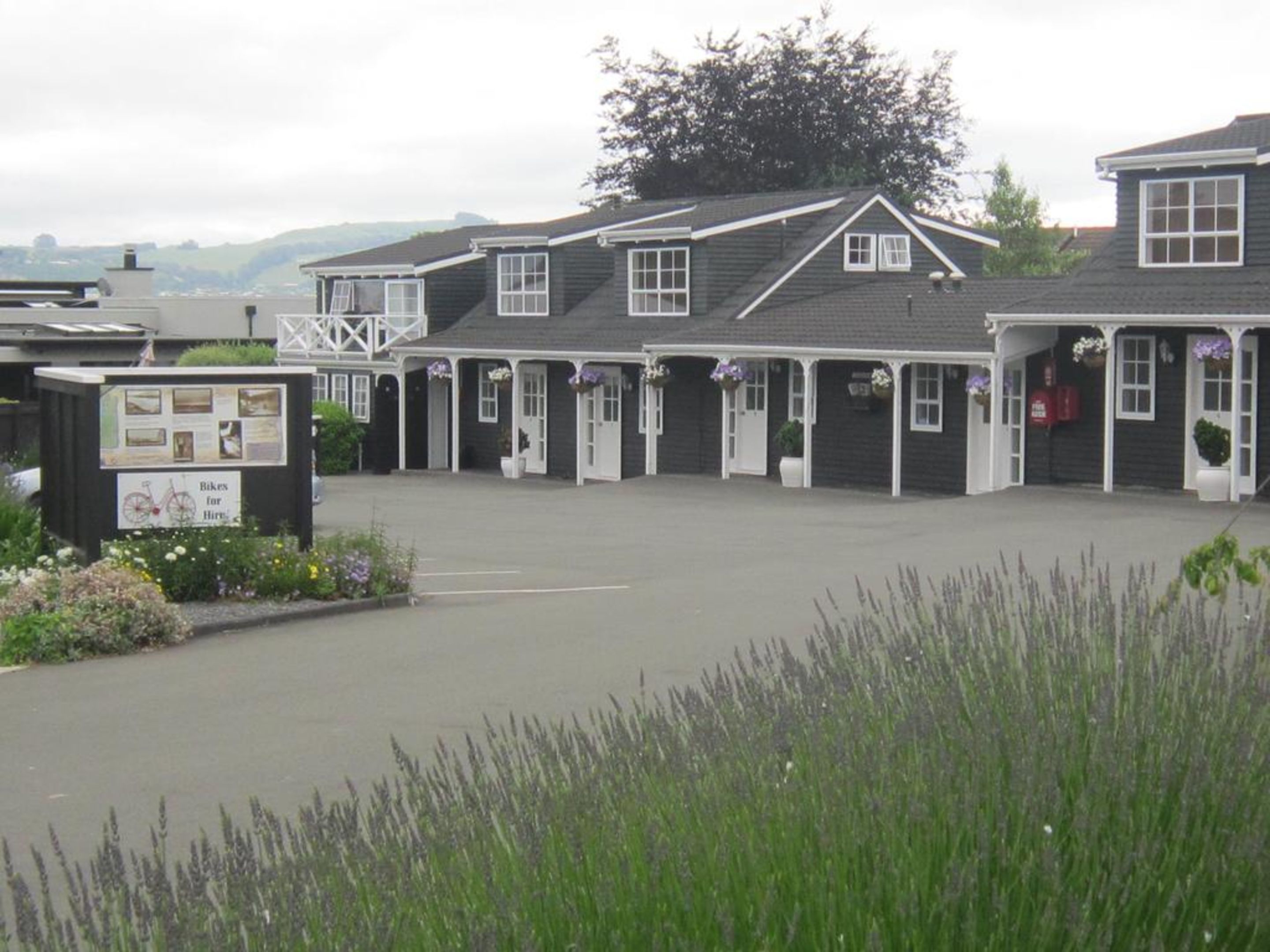 A row of dark-colored, single-story buildings with white trim, likely a hotel or guesthouse, featuring multiple doors and windows, and a paved courtyard.