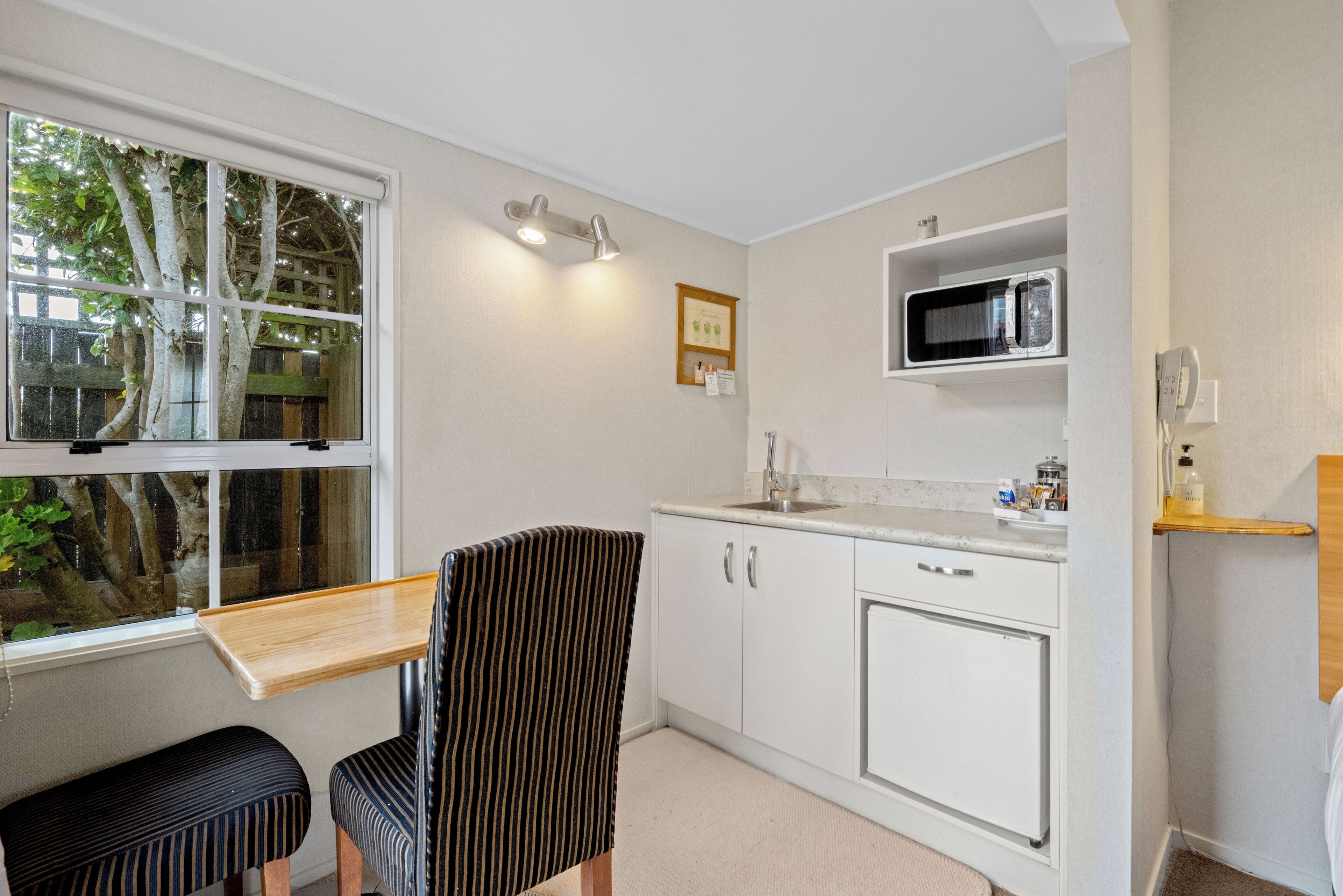 A compact kitchen with white cabinets, a microwave, and a small window overlooking a tree.