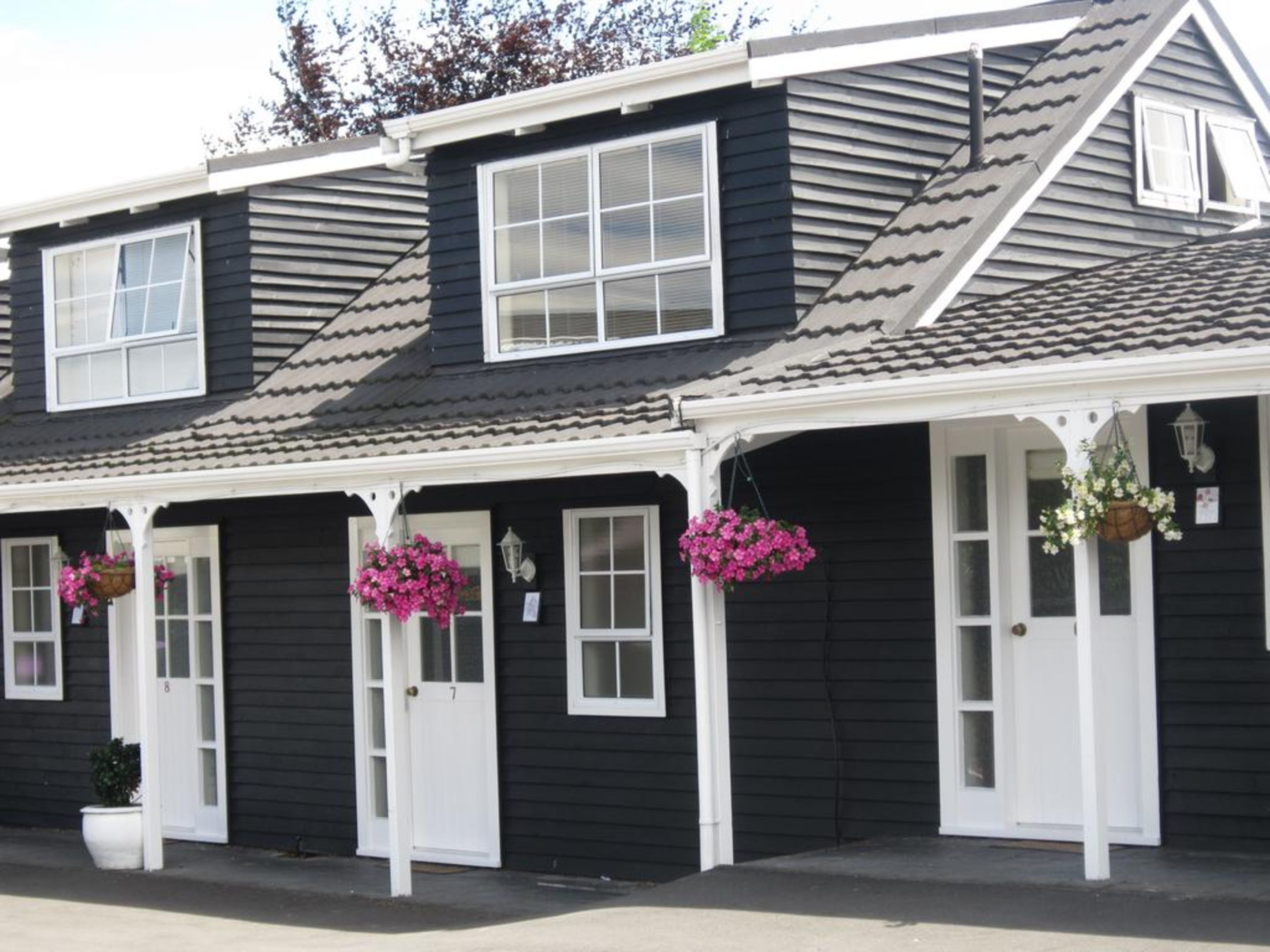 A row of black buildings with white trim and multiple windows, each with a door and hanging flower baskets.