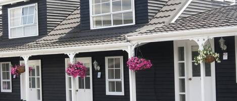 Uma fileira de edifícios pretos com detalhes brancos e várias janelas, cada um com uma porta e vasos de flores pendurados.