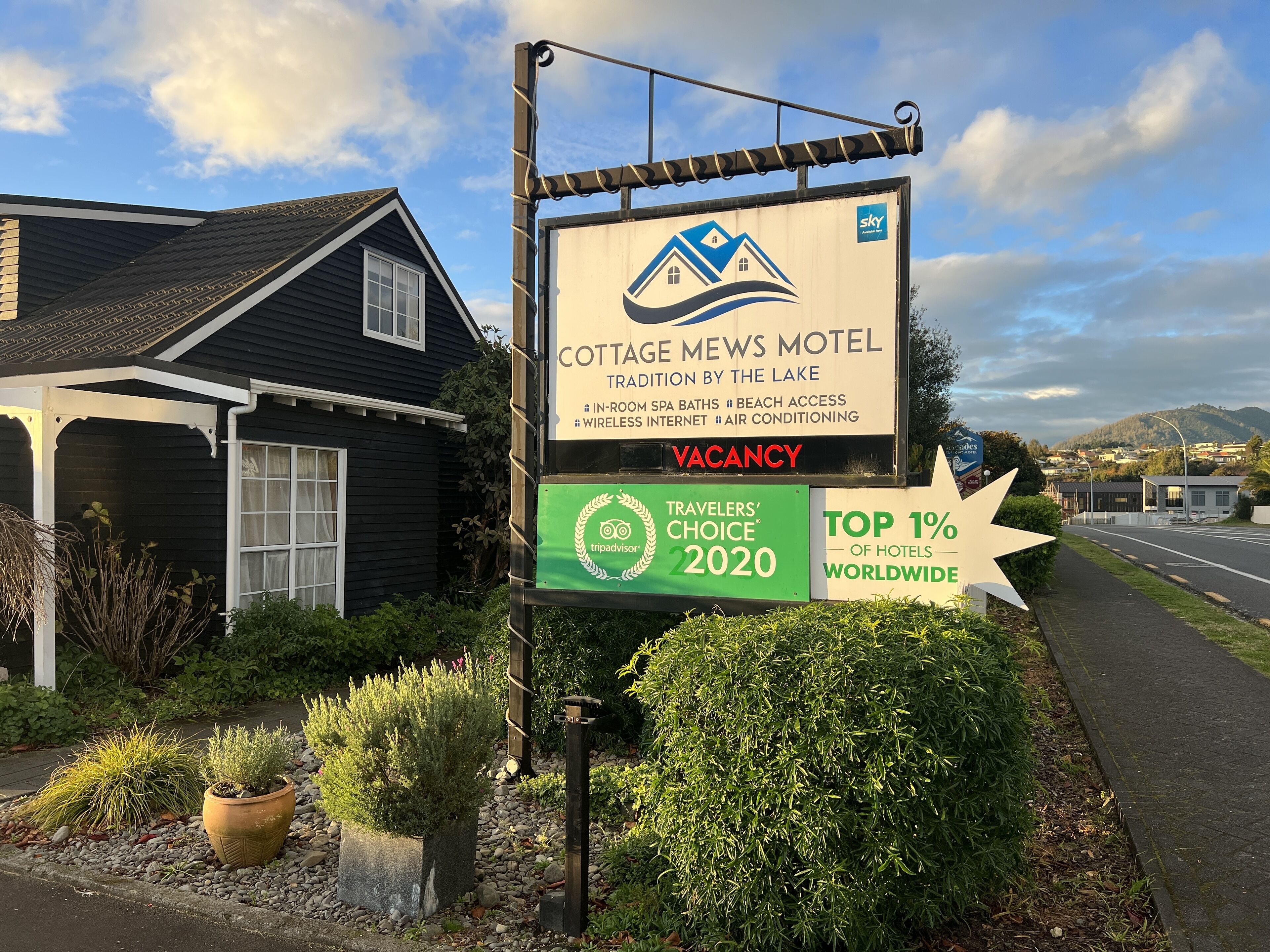 A sign for Cottage Mews Motel advertising amenities like in-room spa baths, beach access, and air conditioning.