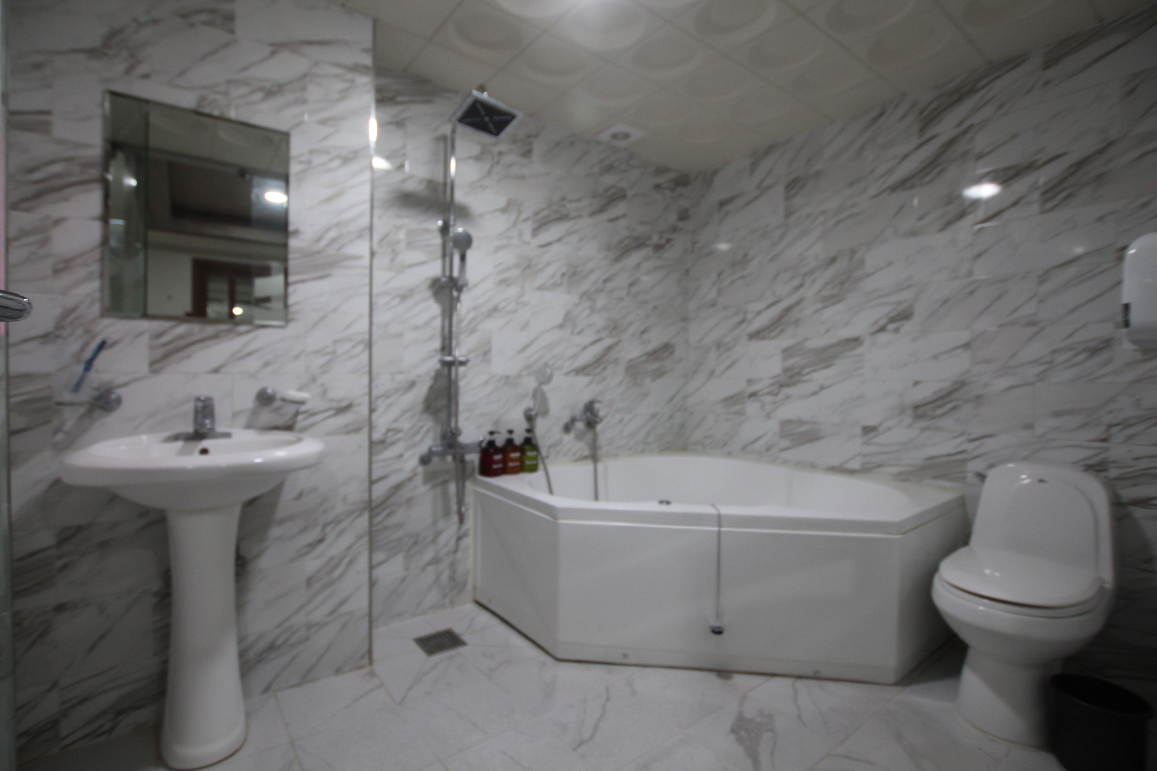 A bathroom with a marble floor, a pedestal sink, a freestanding bathtub, and a toilet.