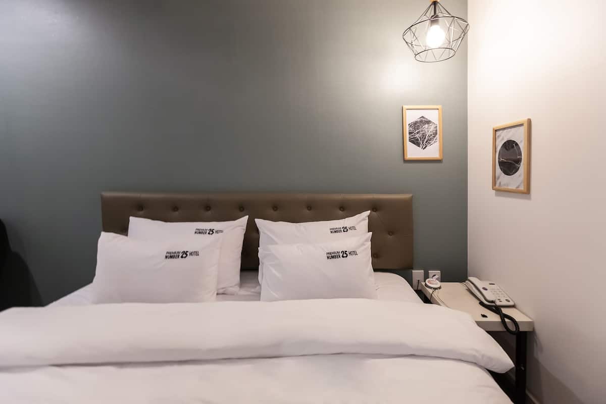 A neatly made bed with white bedding and two pillows, a bedside telephone, and a wall-mounted light fixture.