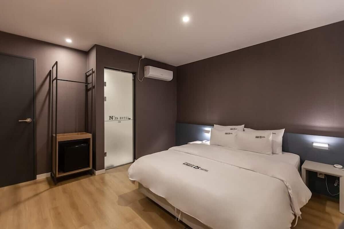 A hotel room with a bed, bedside table, and a wall-mounted air conditioning unit.