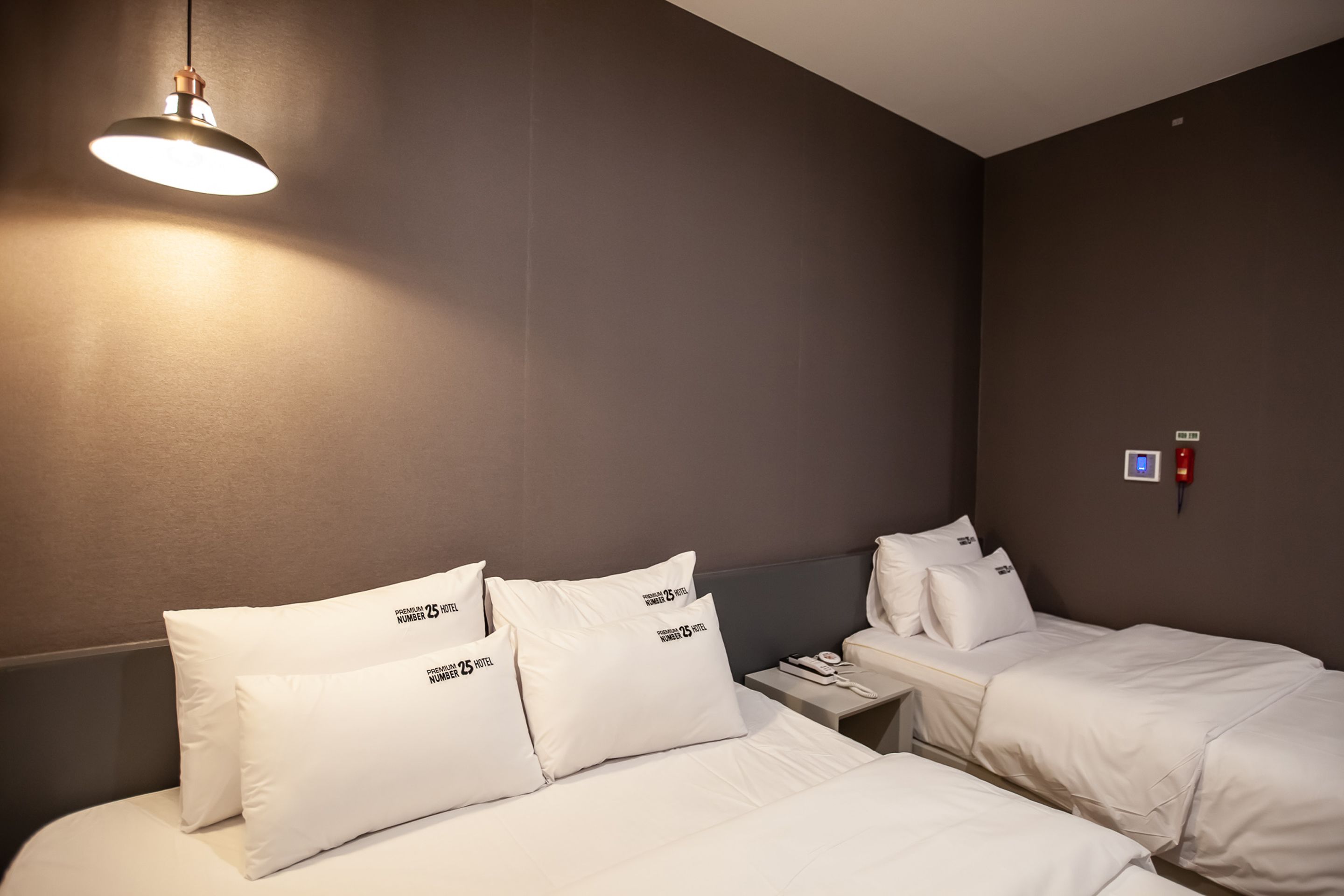 A hotel room with two beds, white bedding, a bedside table with a phone, and a wall-mounted light fixture.