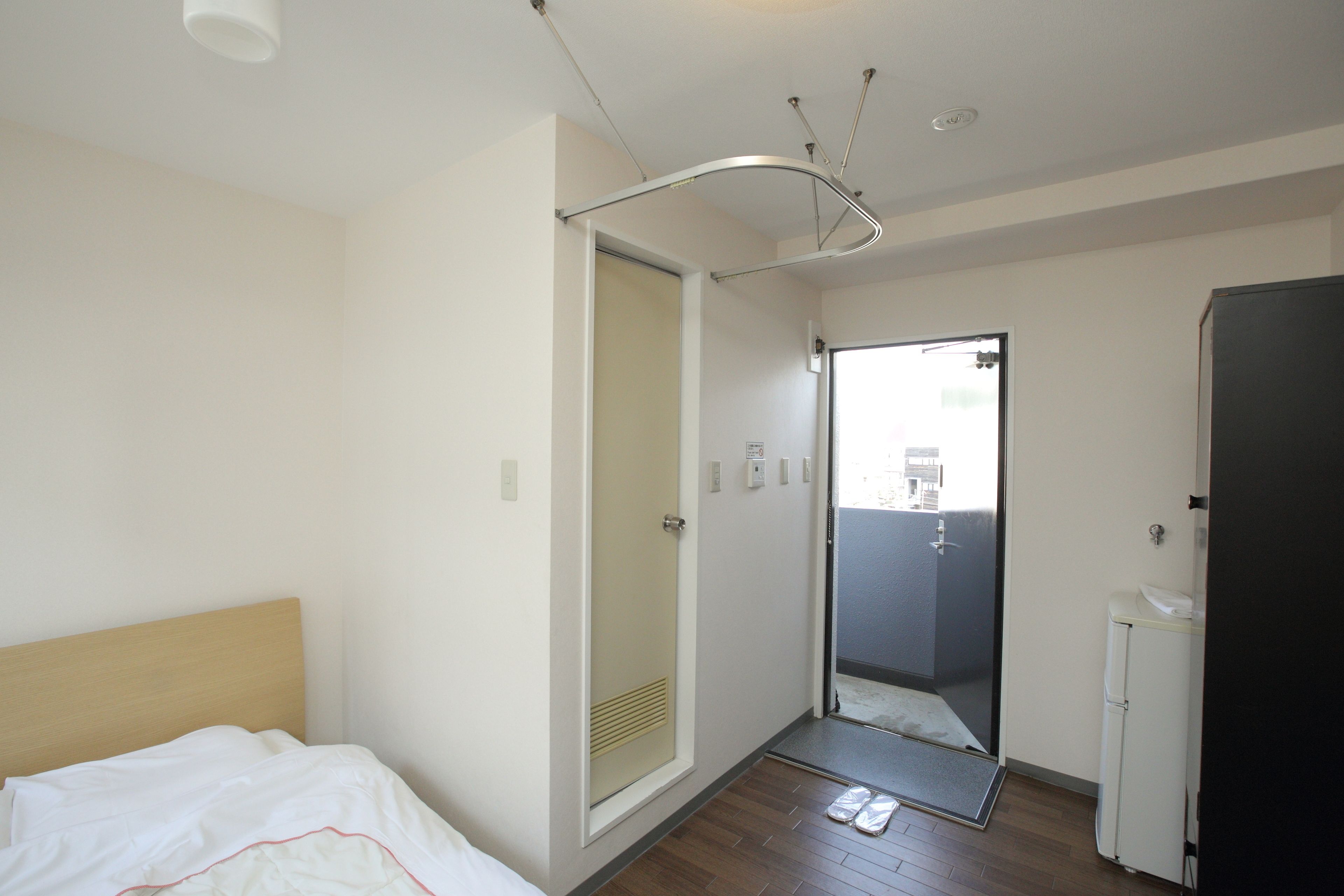 A hotel room with a bed, a door leading to a bathroom, a small refrigerator, and a ceiling light fixture.
