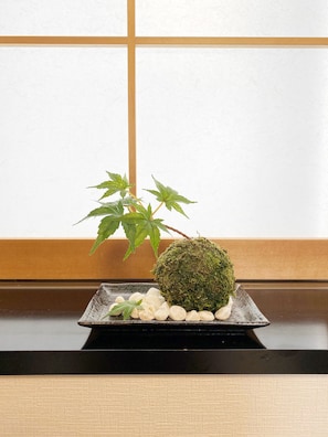 A traditional Japanese-style room with tatami flooring, a shoji screen, and a low table with a bonsai and a moss ball.