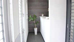 A narrow hallway with a reception desk, a potted plant, and a door on the right. - OUCHI HOTEL Yokogawa (Hiroshima)
