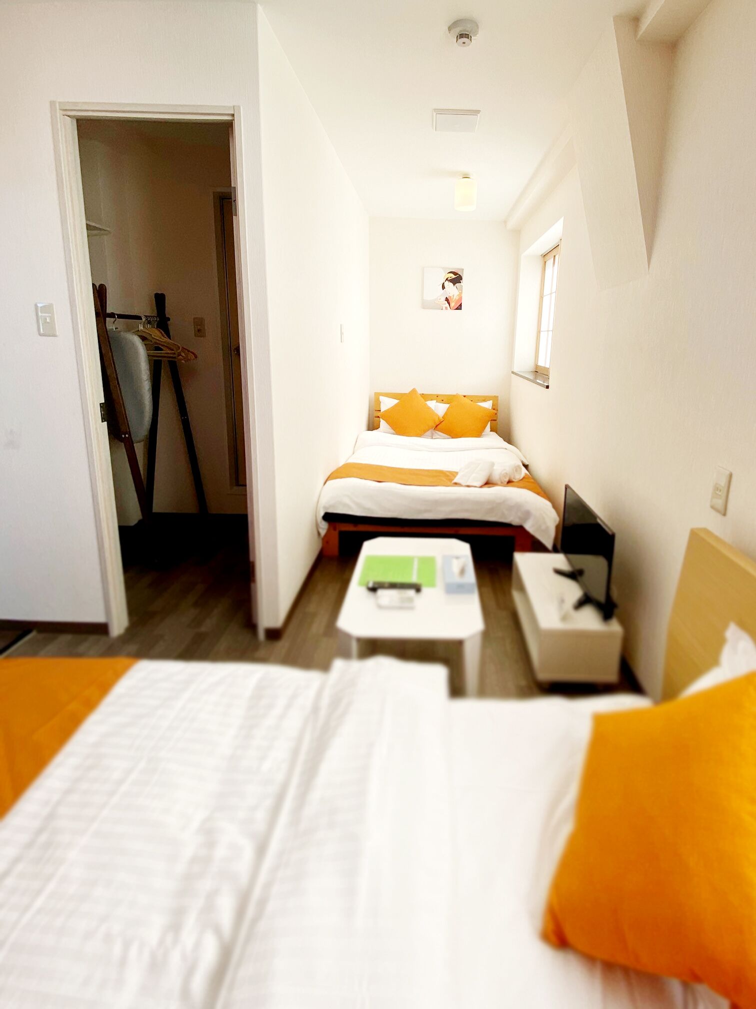 A hotel room with two beds, a small table, a bedside table, a mirror, and a window.