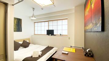 A hotel room with a bed, a desk, a window, a painting, and a ceiling light fixture.