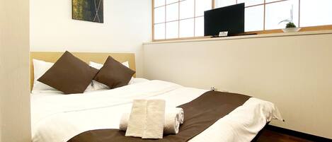 A hotel room with a bed, pillows, a flat-screen TV on a shelf, and a painting on the wall.