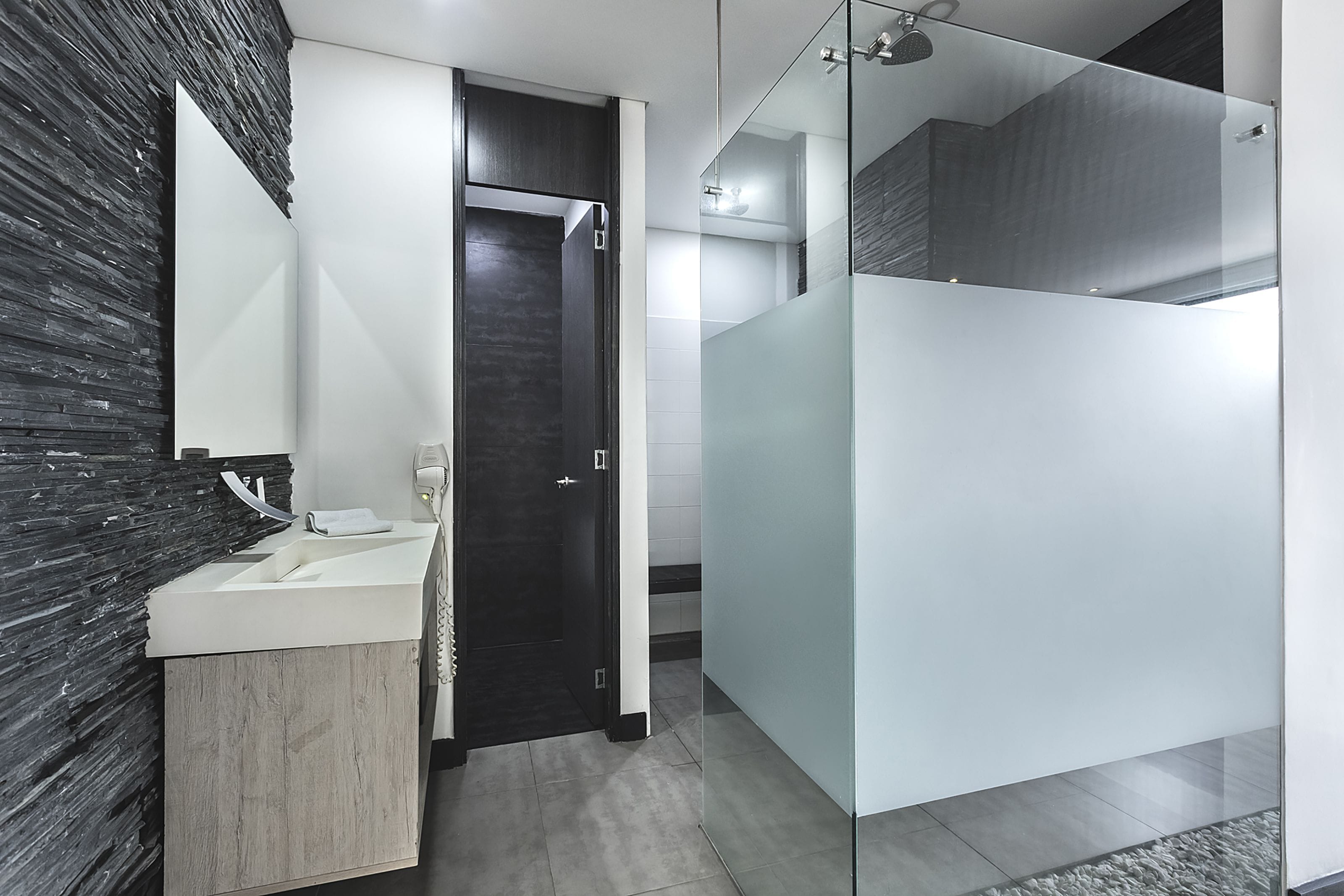 Un baño moderno con una puerta de madera oscura, un lavamanos blanco y un box de ducha de vidrio.