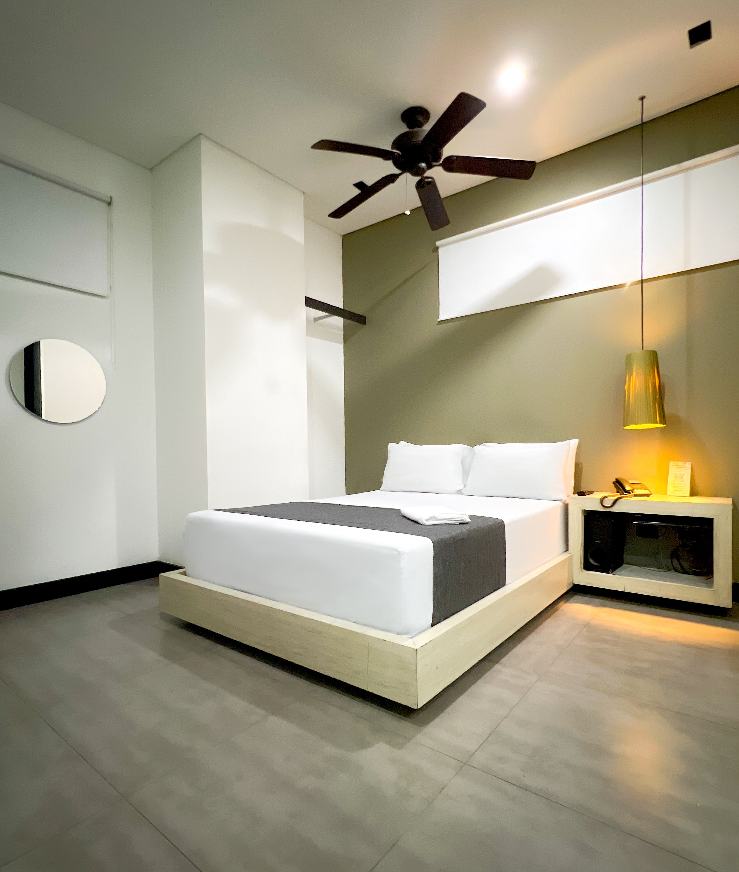 A modern bedroom with a bed, a ceiling fan, a bedside table with a lamp, and a wall-mounted mirror.