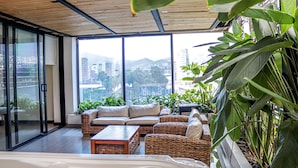 A modern living room with a large window, wicker furniture, and indoor plants. - Hotel 47 Medellin Street (Medellín)