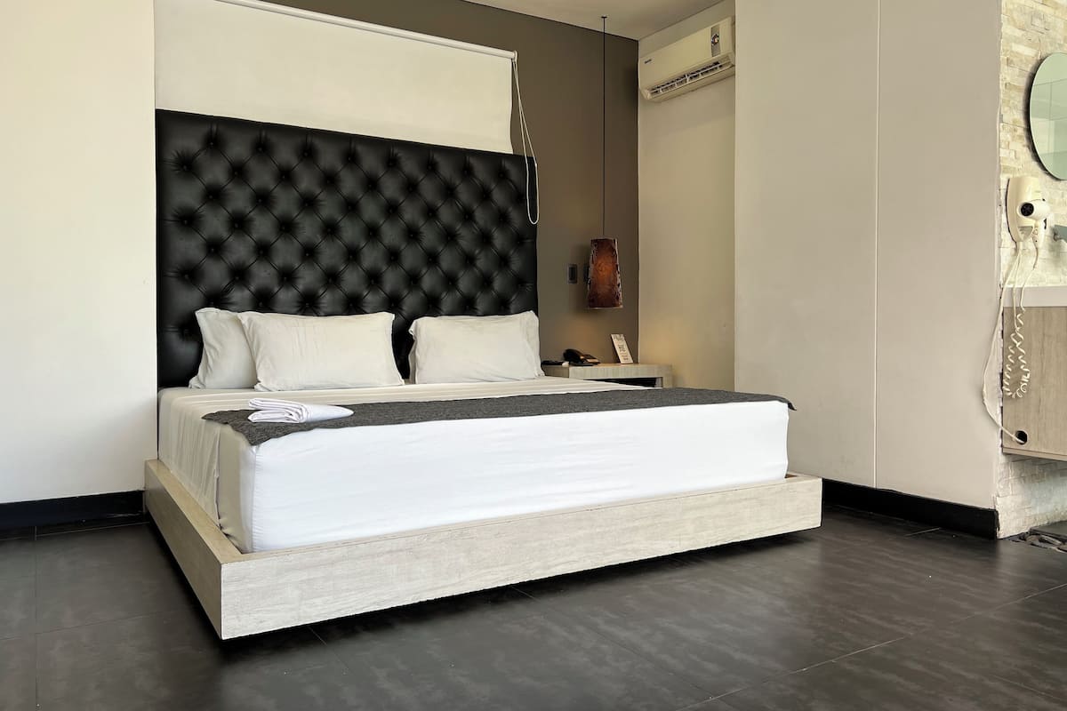 A modern bedroom with a tufted headboard, a bedside table with a lamp, and a built-in air conditioning unit.