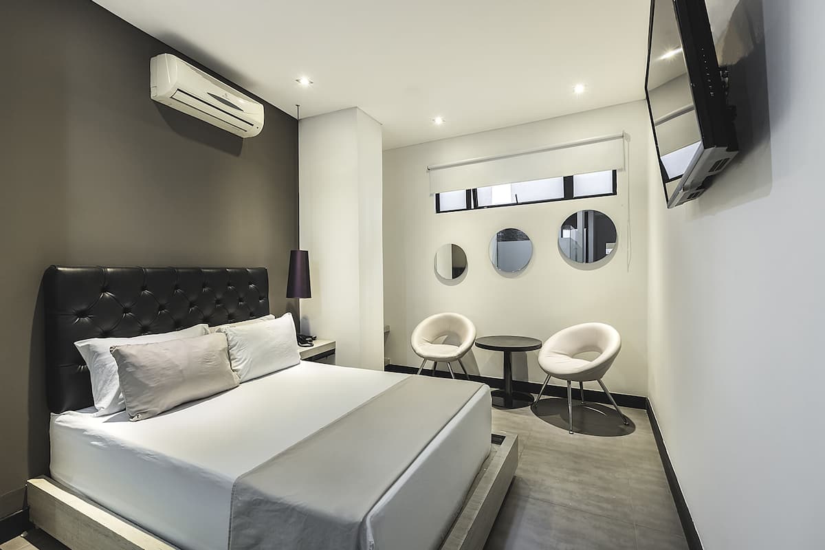 A modern hotel room with a large bed, a flat-screen TV mounted on the wall, and two round mirrors above a small table and chairs.