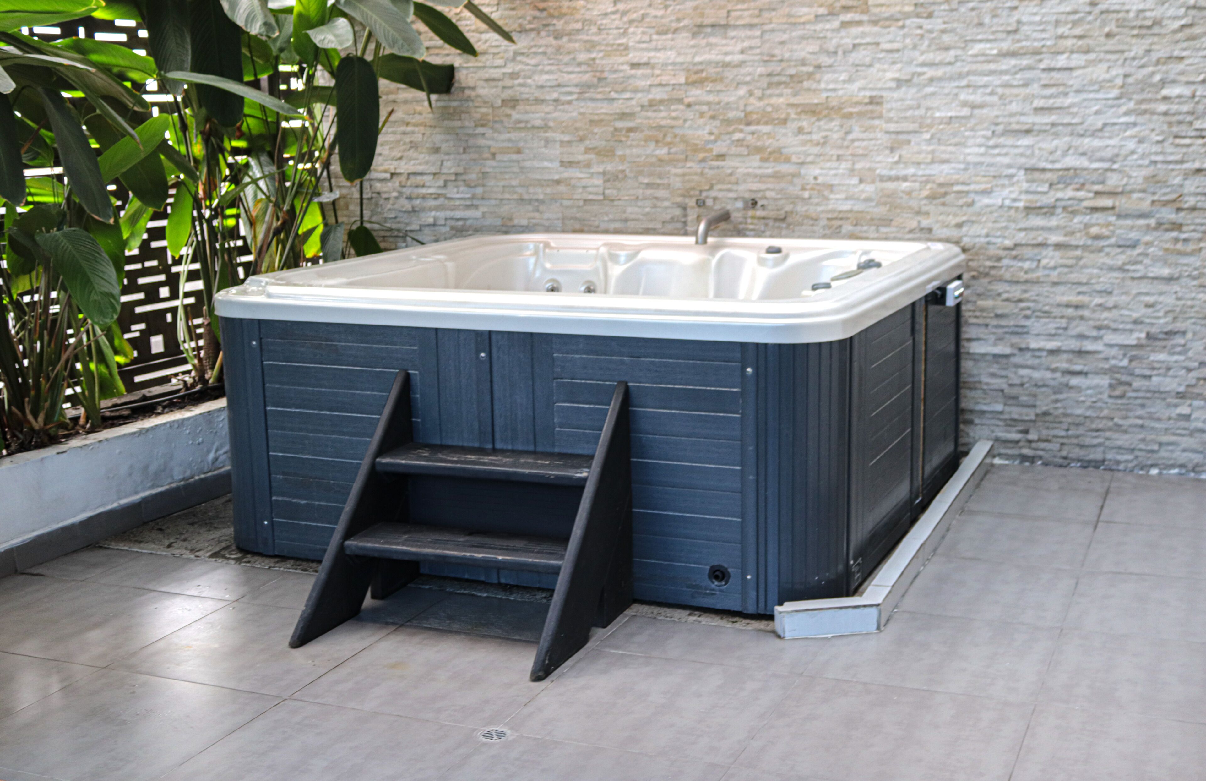 A hot tub with steps leading up to it, set against a stone wall and surrounded by greenery.
