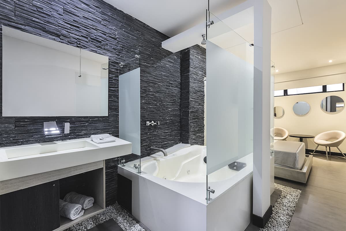 A modern bathroom with a large mirror, two sinks, a bathtub, and a shower.