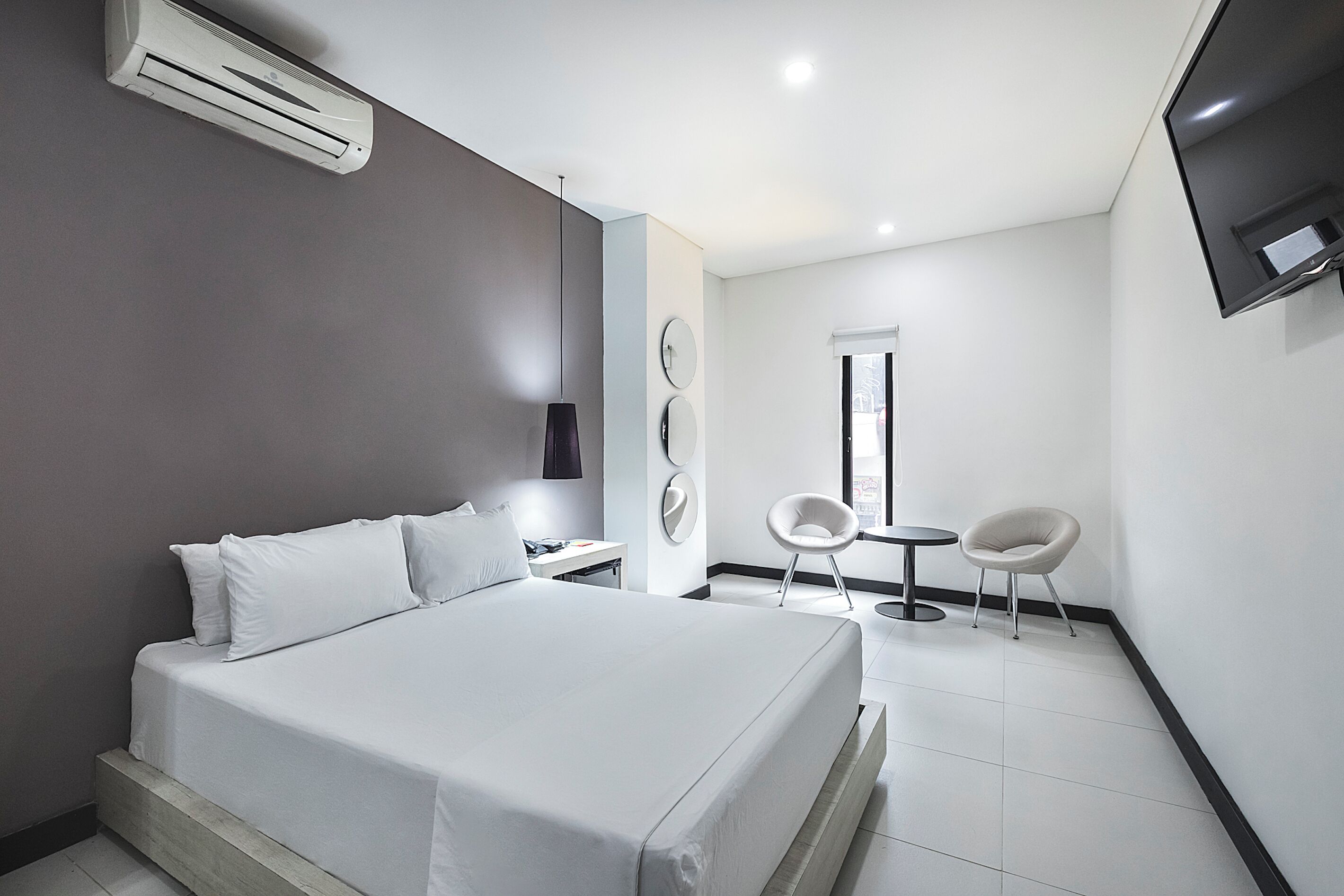 A modern hotel room with a large bed, a desk, two chairs, and a TV mounted on the wall.