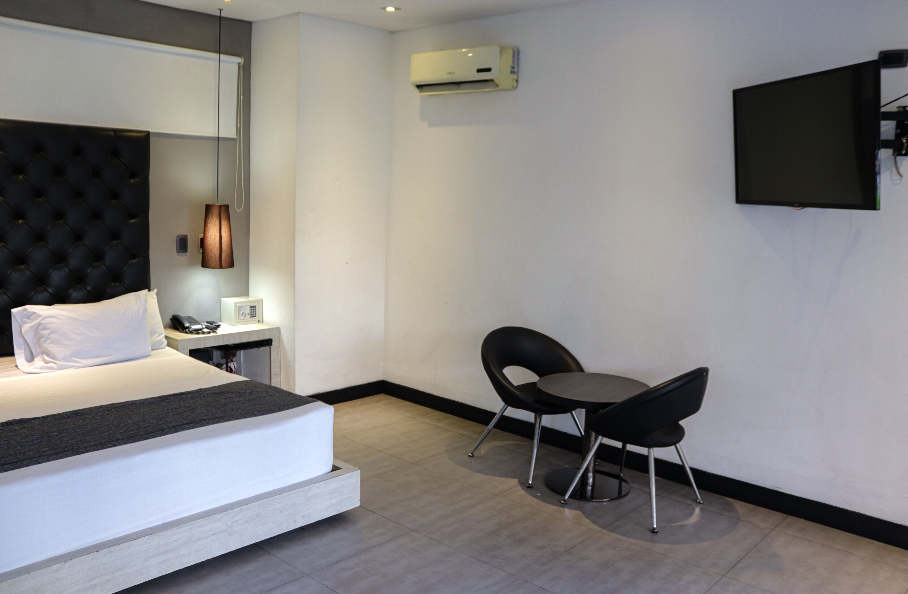 Een moderne hotelkamer met een bed, nachtkastje, lamp, airconditioning, televisie en twee stoelen.