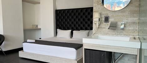 A modern hotel room with a large bed, a round mirror, a built-in vanity, and a city view.
