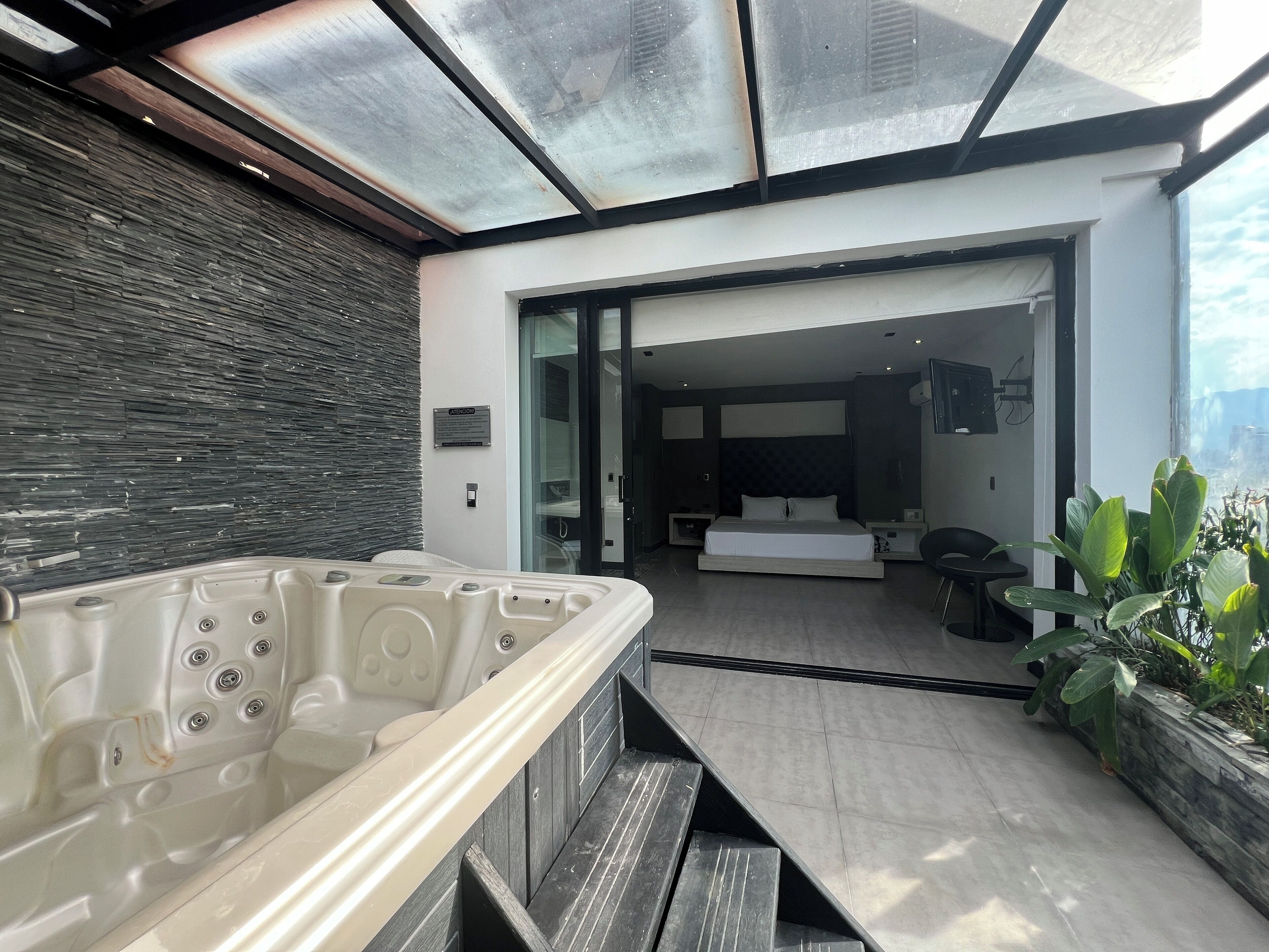 Un spa moderno con un jacuzzi, un banco de madera y vistas al dormitorio contiguo.